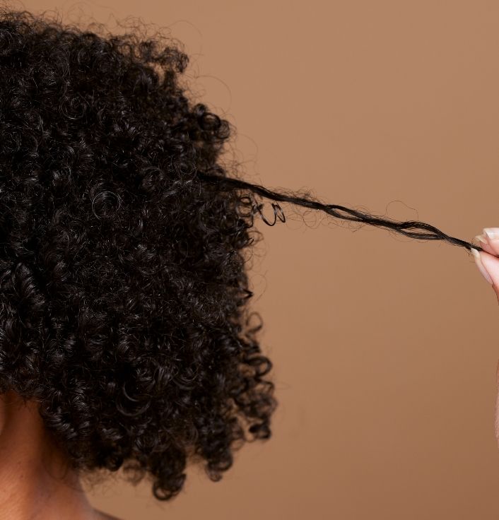 Close-up of a woman examining the ends of her healthy 4C hair.