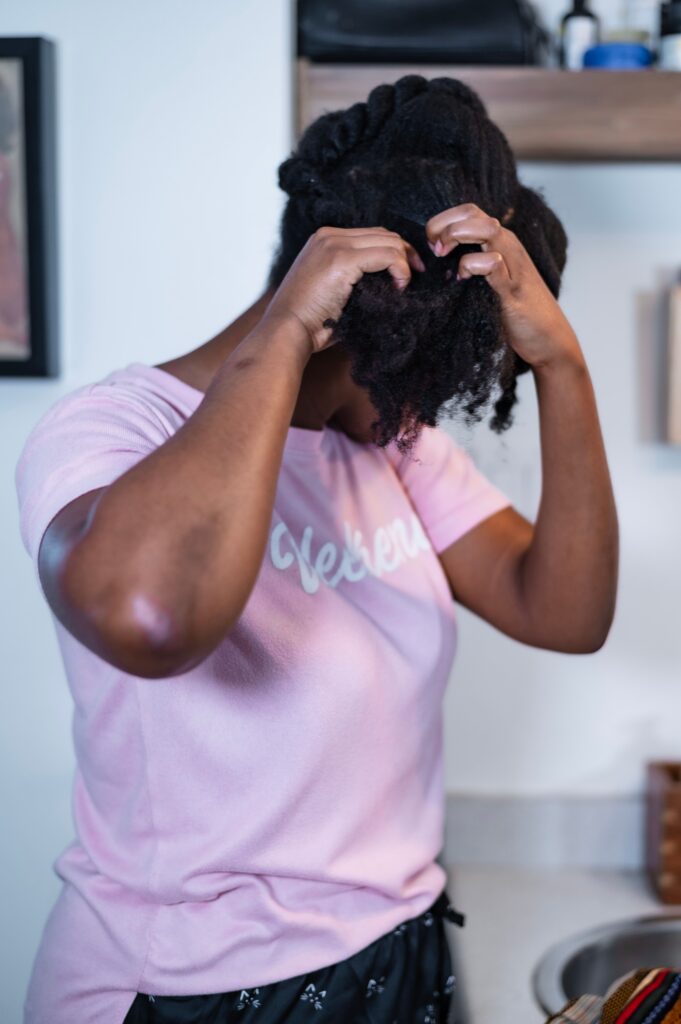 Black woman parting her 4C hair to examine the condition of her scalp.