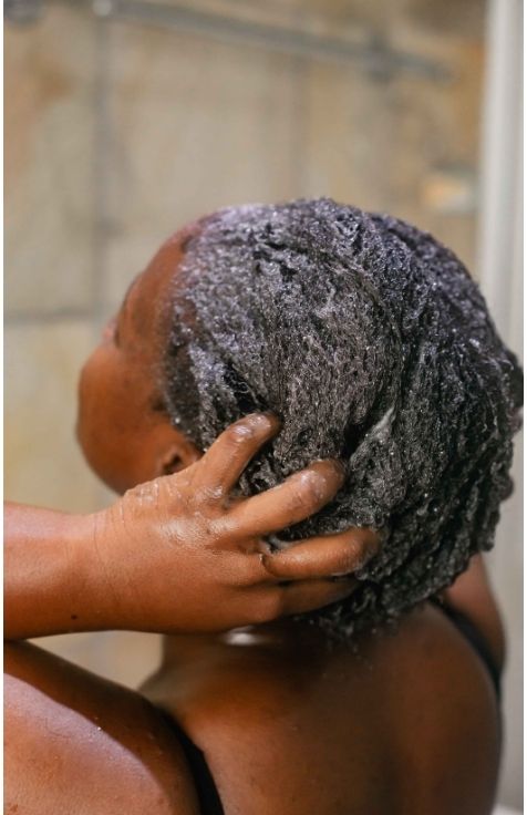 Black woman washing her 4C hair during her weekly wash day routine.