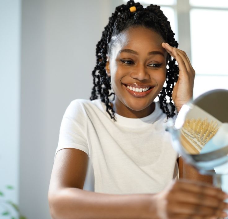 Black woman smiling while checking her clean, healthy scalp.