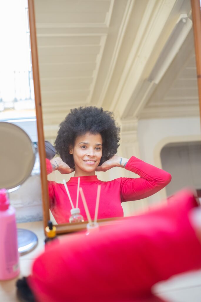 Black woman smiling while caring for her natural 4C hair during a relaxed self-care day.