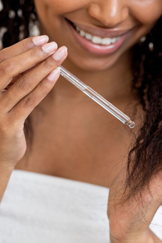 Black woman applying nourishing hair oil to healthy natural hair.