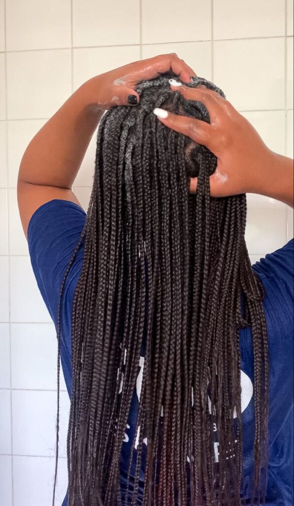 Black woman cleansing her scalp while wearing knotless braids protective styling.