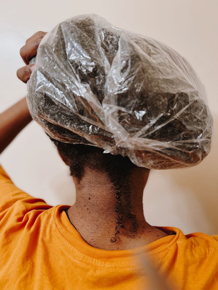 Black woman wearing a shower cap while deep conditioning her natural 4C hair.
