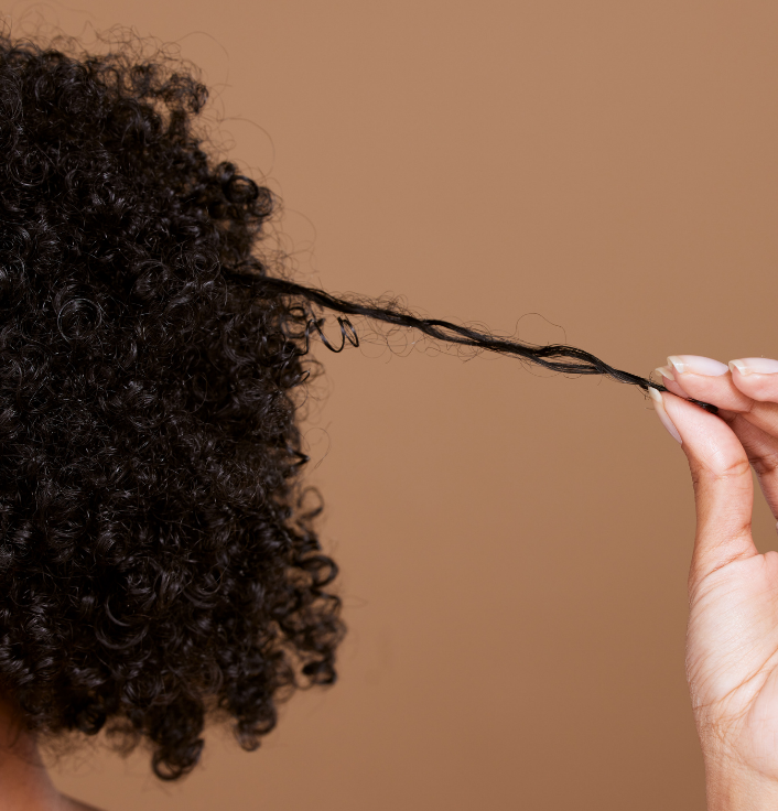 Black woman with healthy natural hair gently holding her stretched curls.
