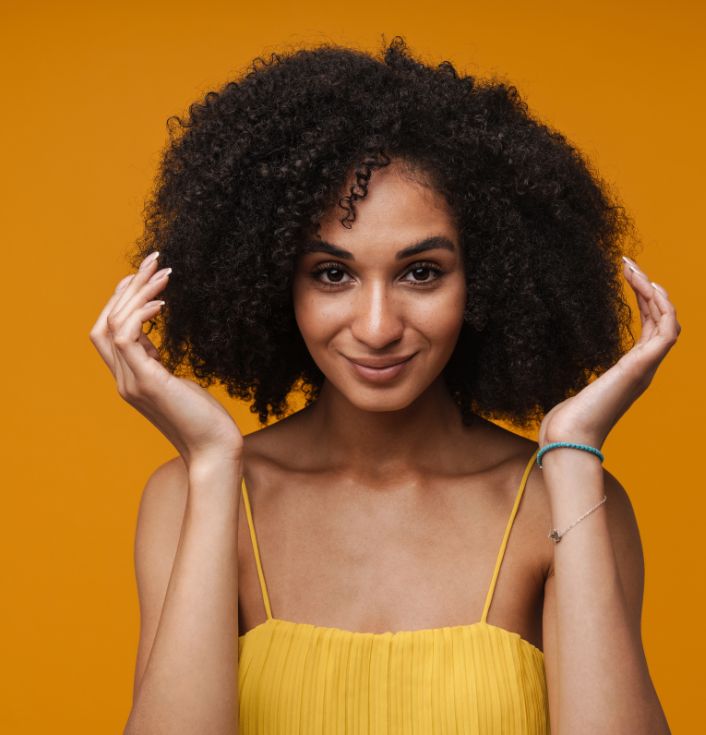 Black woman smiling while touching her healthy, moisturized 4C hair.