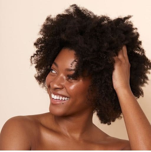 Black woman smiling while touching her freshly washed and moisturized 4C hair after her wash day routine.