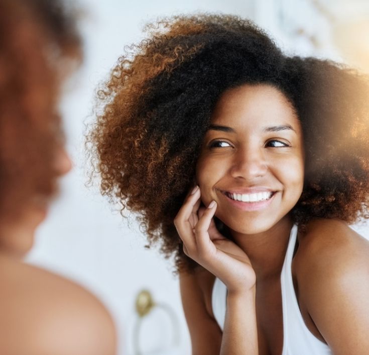 Black woman smiling confidently with healthy, freshly washed natural 4C hair.