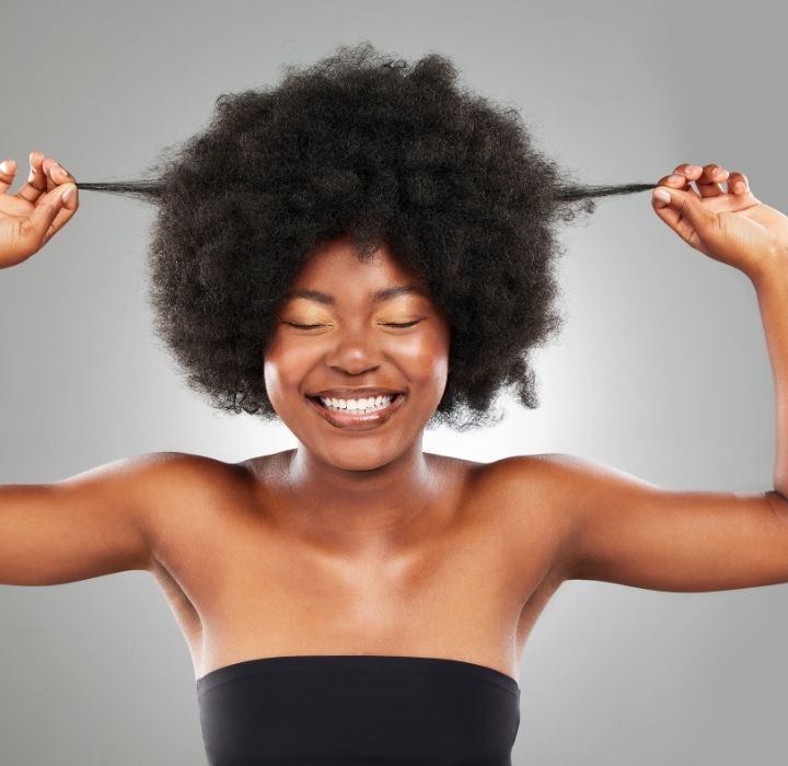 Beautiful Black woman with long healthy natural 4C hair smiling confidently.