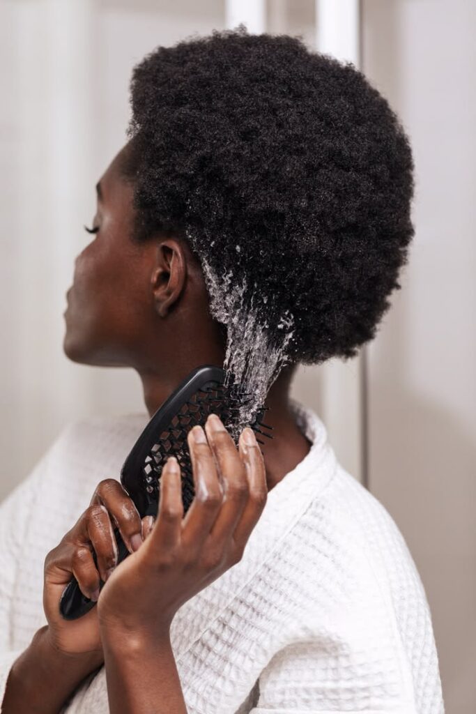 Black woman applying moisturizer to the ends of her healthy 4C hair.