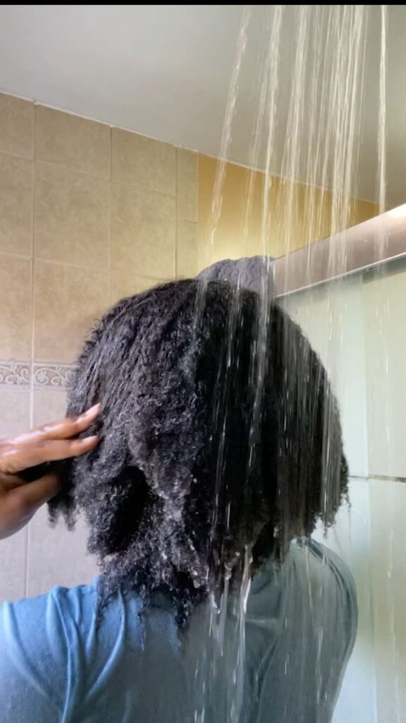 Black woman rinsing deep conditioner from her healthy 4C hair.