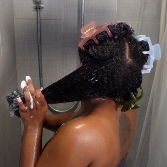 Black woman applying conditioner through freshly washed natural 4C hair.
