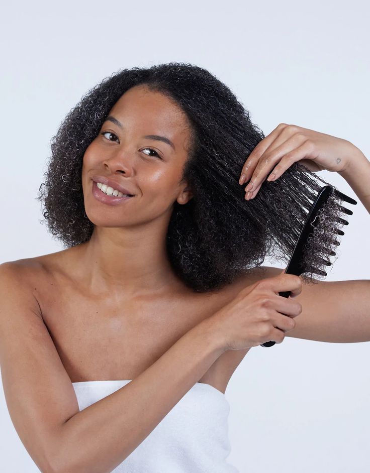 Black woman gently detangling natural 4C hair in small sections with conditioner and a wide-tooth comb