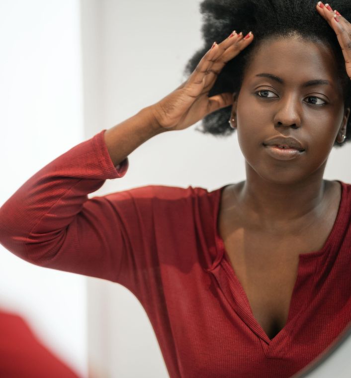 Black woman examining her hairline and edges in a mirror