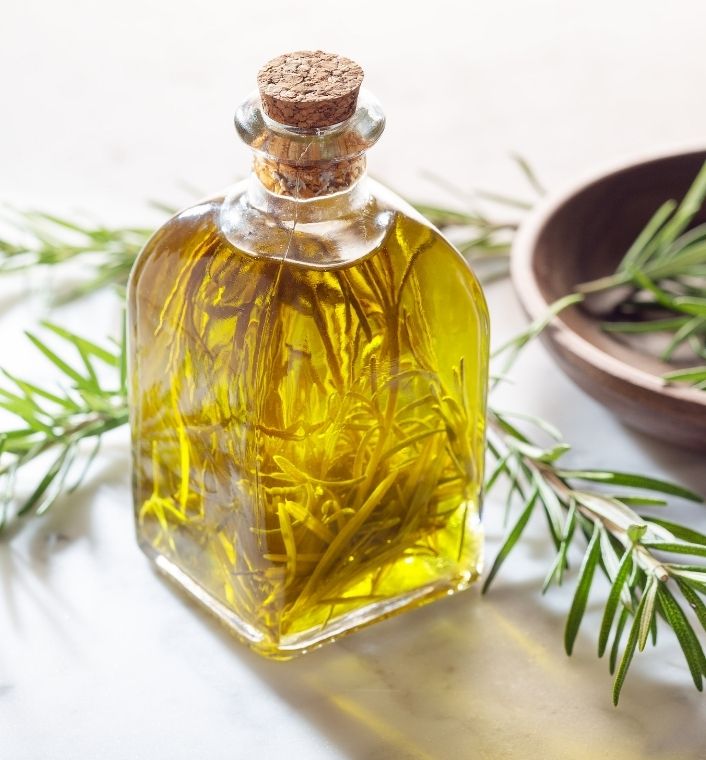 Rosemary sprigs beside a bottle of infused carrier oil.