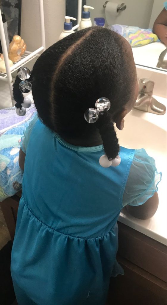 Young Black child wearing two neat braided pigtails protective styles