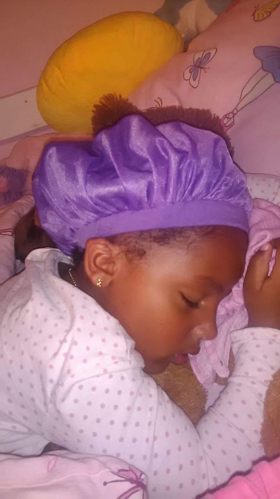 a child wearing satin hair bonnet in bed to protect hair from friction