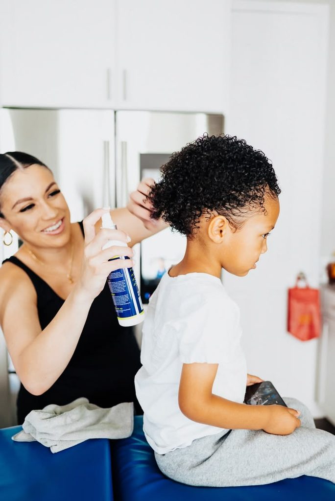 Parent moisturizing a kid's damp 4C natural hair after washing as part of wash day routine