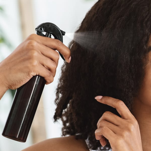 Woman applying moisturizer to natural hair during transition