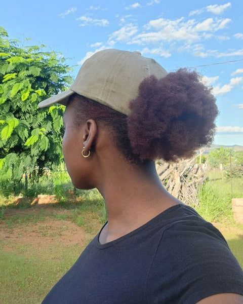 Woman protecting natural 4C hair outdoors with a stylish hat during spring
