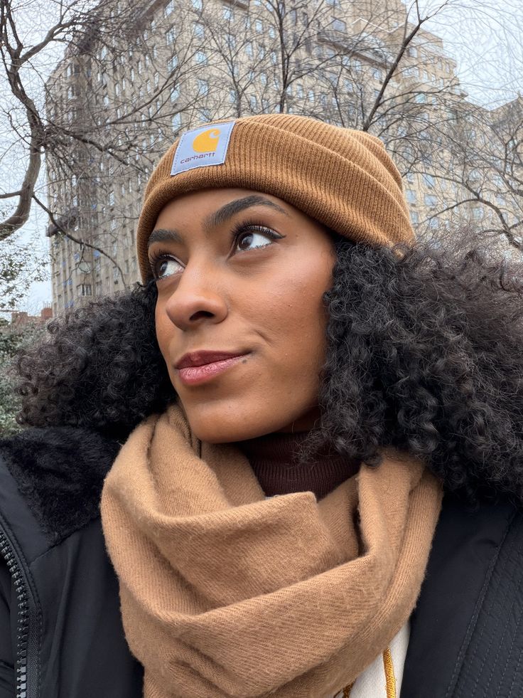 Black woman wearing a winter hat with a satin scarf underneath to protect natural hair