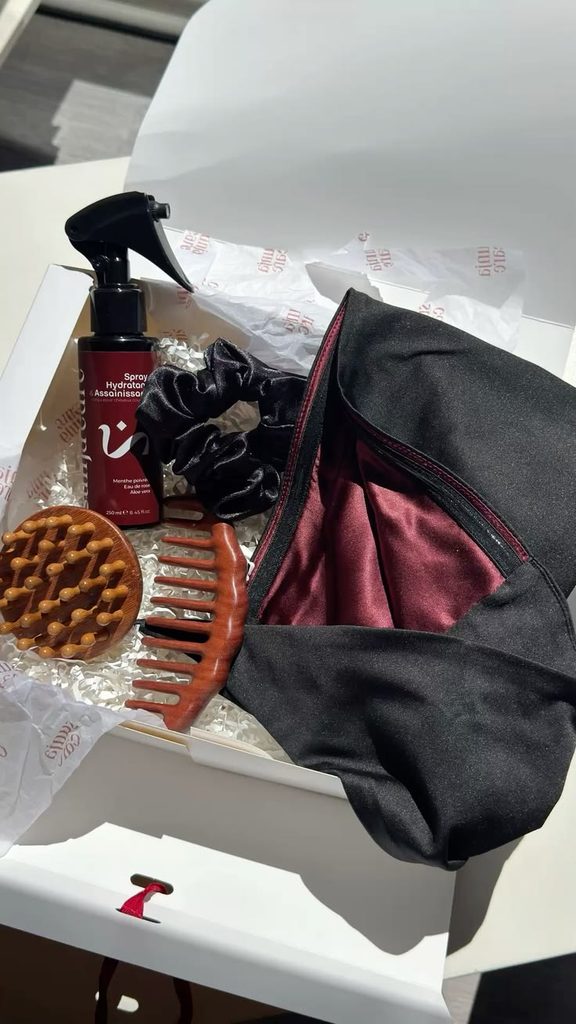 Flat-lay of winter hair care products beside a satin scarf, wide-tooth comb, and spray bottle